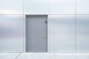 Closed, gray hollow steel door on paneled wall