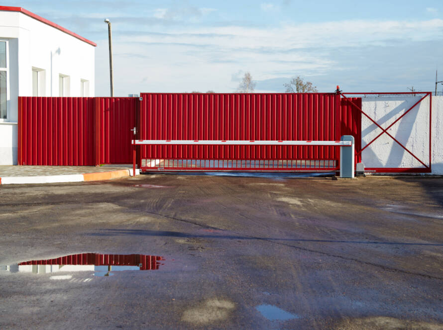 Red sliding gate with arm and stone wall