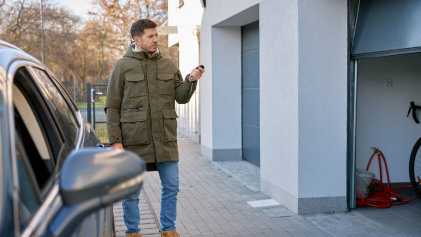 Homeowner pushing garage door remote next to parked car