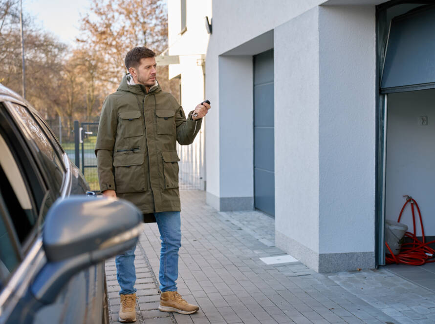 Homeowner pushing garage door remote next to parked car